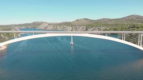 Aerial view of concrete highway spectacular bridge over the sea with a sail boat. Clear water and car traffic concept