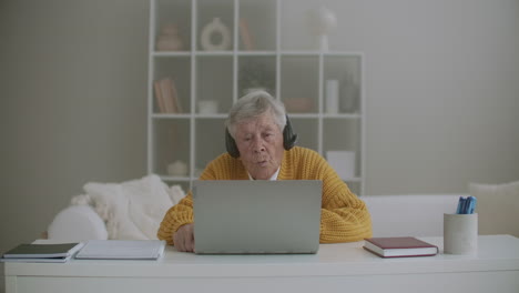 Mujer-Mayor-Con-Computadora-Portátil-Llamando-A-Un-Teléfono-Inteligente-En-Casa.-Anciana-Haciendo-Una-Videollamada-En-El-Portátil-Sonriendo-Y-Hablando-Alegremente-En-El-Interior-De-Un-Acogedor-Apartamento.-Doctor-Videollamada-Paciente-Mayor