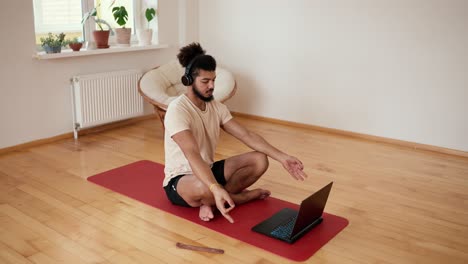 Mixed-race-man-in-headphones-meditates-in-front-laptop-with-instructor