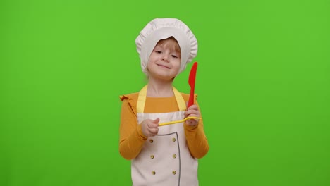 niña vestida de chef cocinero con tenedor y cuchillo, agitando la cabeza de aprobación en el fondo de la llave cromada