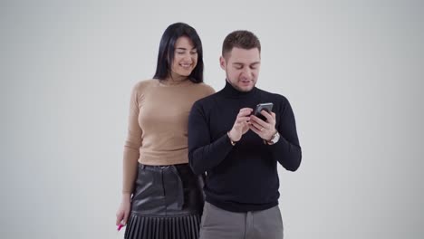 smiling young couple in studio. business partners standing together and looking into the phone. handsome man and attractive woman on the white background.