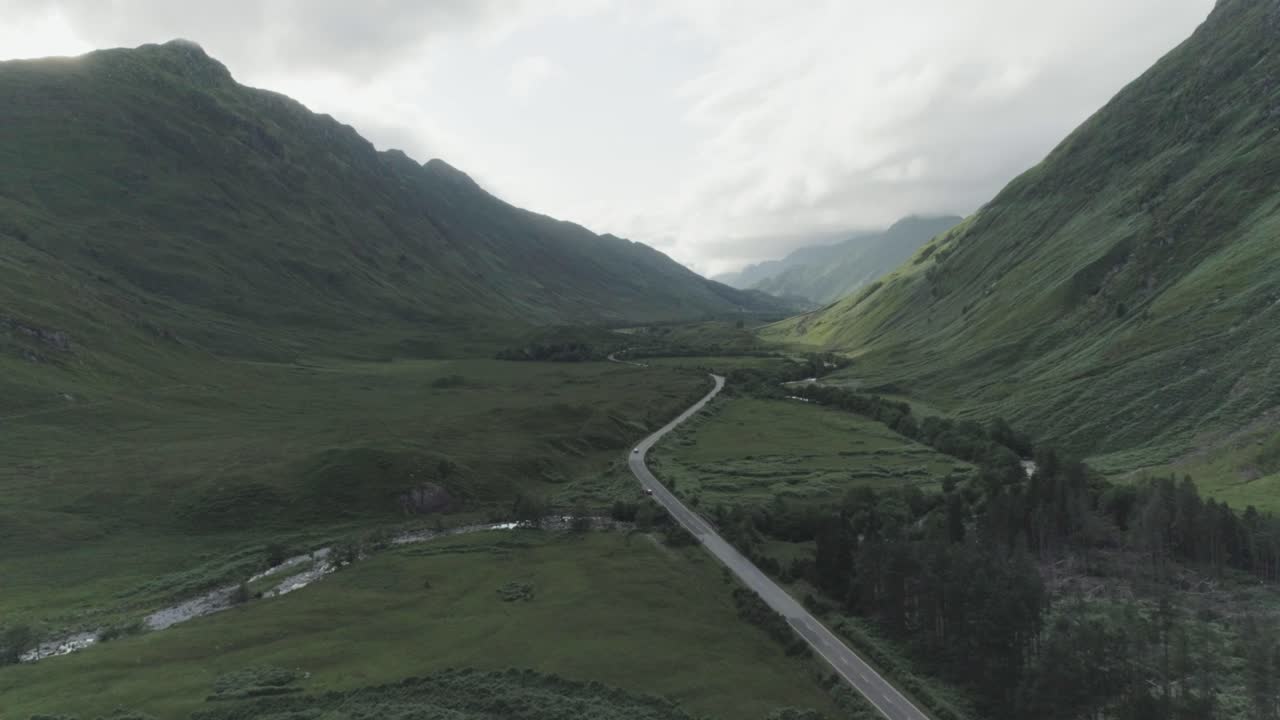 Dramatic wide drone shot showing the north coast 500 route which runs between two huge mountains with traffic flowing below and cloud cover in the background