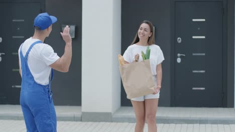 beautiful woman meets a delivery man who gives her a shopping package with food beside her home. food delivery. concept of courier, home delivery, online shopping