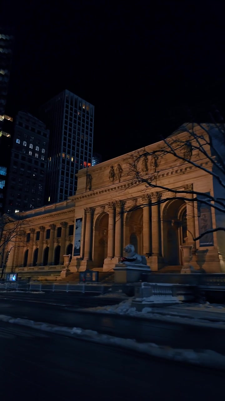 New York, USA, 20 dicembre 2025: Facciata della New York Public Library illuminata di notte. Alberi spogli incorniciano l'esterno in pietra classica accanto a chiazze di neve a Manhattan