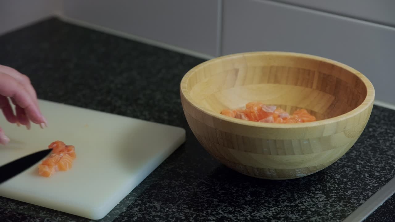 Static shot of woman hands putting raw salmon from her knife into a wooden bowl, interior