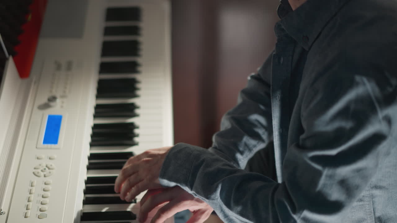 un hombre con una camisa azul tocando un piano blanco con enfoque y concentración. el fondo está borroso, llamando la atención al músico y su interacción con el instrumento