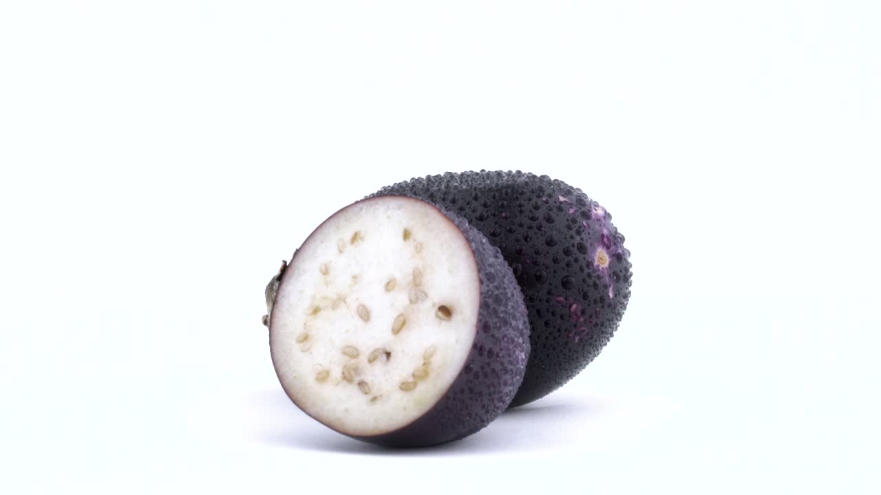 uno y medio de mini berenjena púrpura con gotas de agua. girando en la mesa giratoria. aislado en el fondo blanco. primer plano. macro.