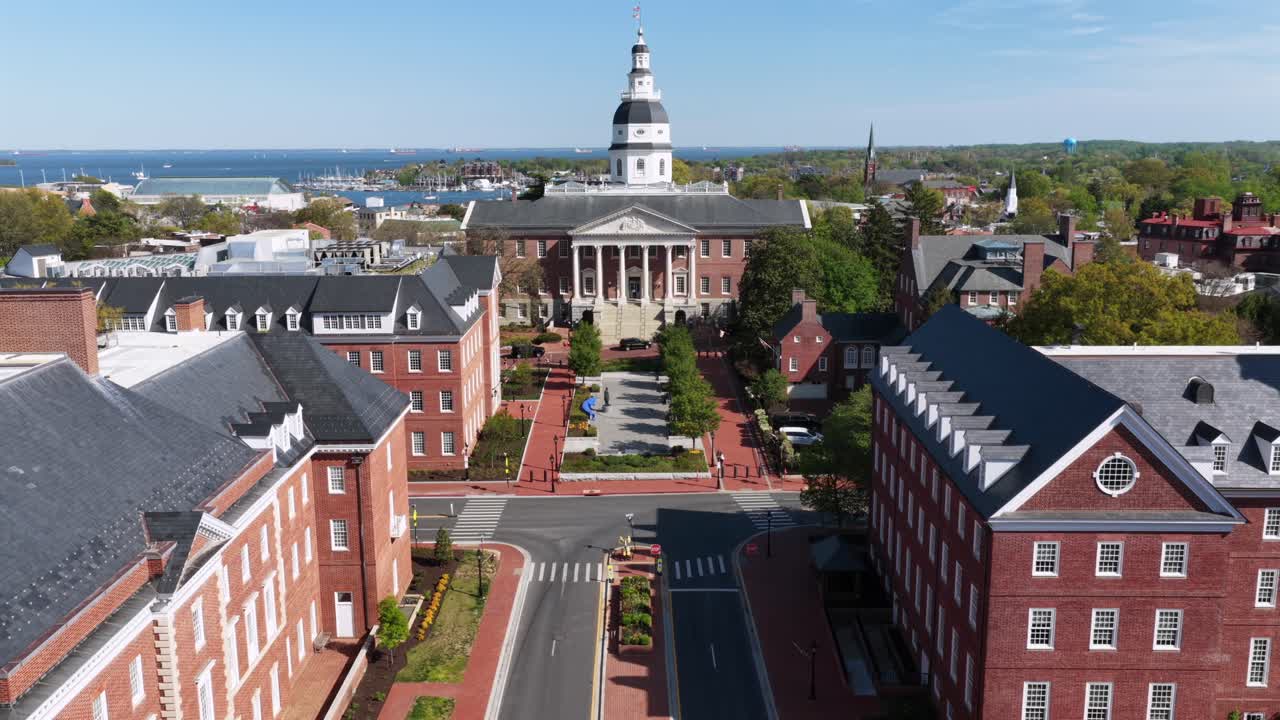 Luftfoto af Maryland State House i Annapolis, Maryland, indrammet af røde murstensbygninger og gader i centrum, med Chesapeake Bay i baggrunden under strålende forårssolskin i den historiske amerikanske hovedstad.