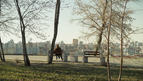 padre e hijo sentados juntos en un banco, mirando el paisaje de la ciudad desde un parque al aire libre, el padre tiene las piernas cruzadas mientras el niño golpea suavemente su pierna