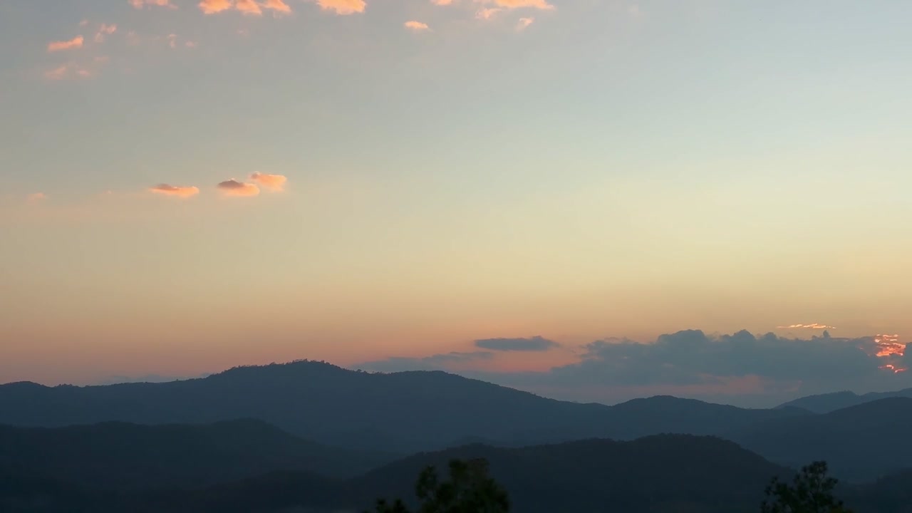 タイのパイにある重なり合う山々の尾根に沈む夕日。地平線には輝くオレンジ色の雲、暖かい夕焼け空を背景にシルエットになった木々