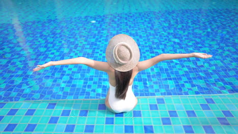 Woman-Sitting-by-the-Blue-Pool-Spreading-Hyper-Flexible-Arms-Rear-View