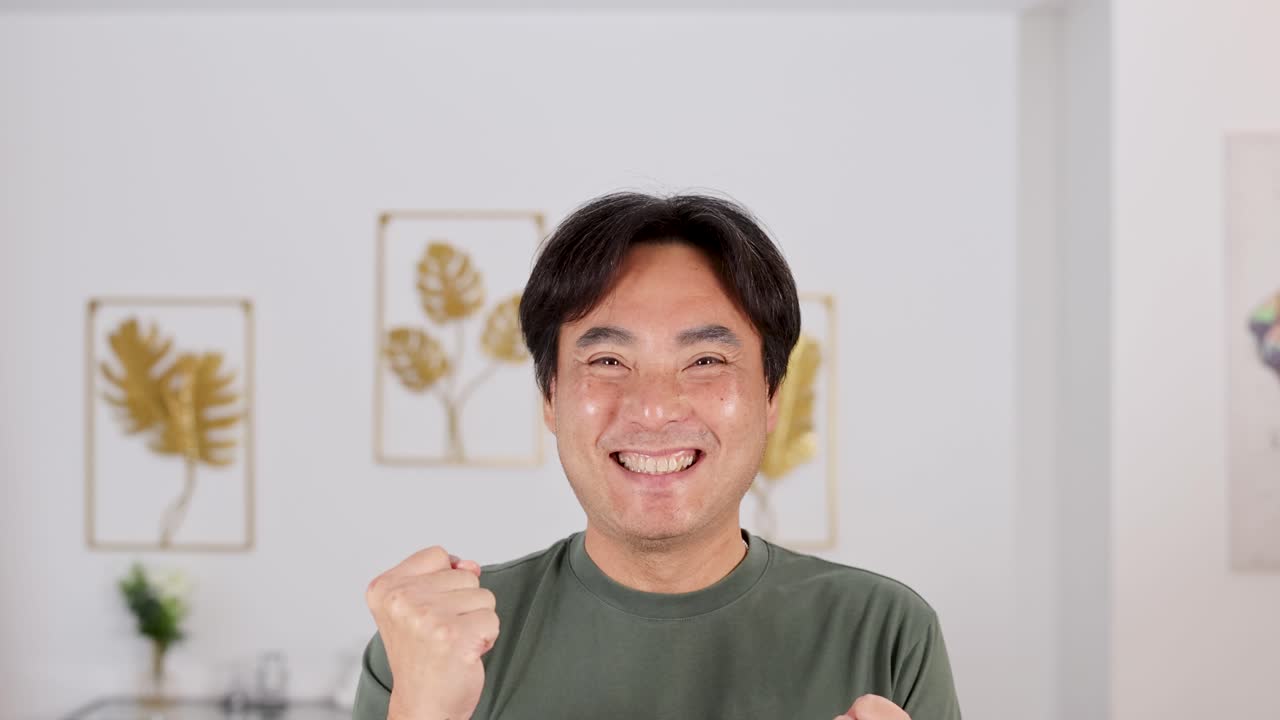 A man expresses excitement with a fist pump in a bright, home environment. Neutral tones and framed art create a cozy atmosphere