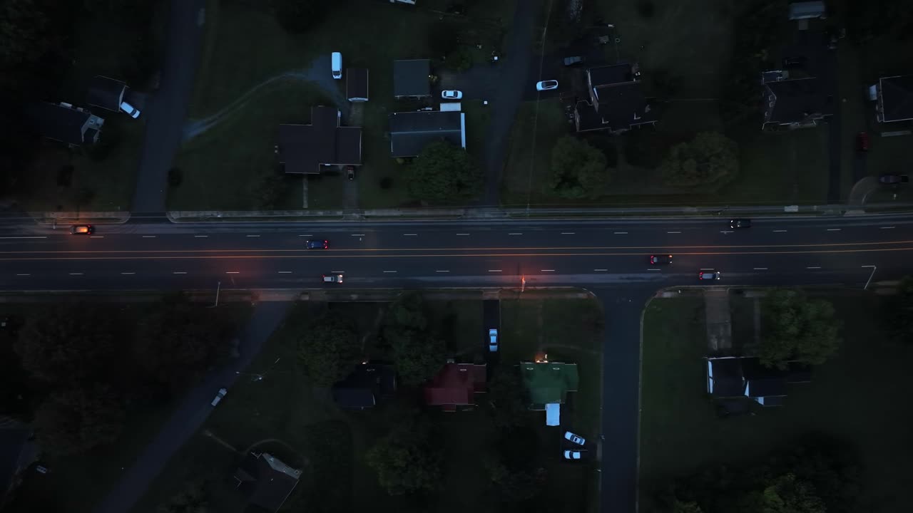 Aerial top down of cars on road at dawn. Traffic scene in American neighborhood. Single family Houses and homes in green suburb at rainy day. Headlights of vehicles on road