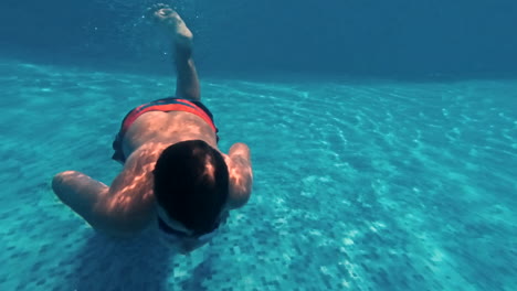 young guy swims underwater in a swimming pool