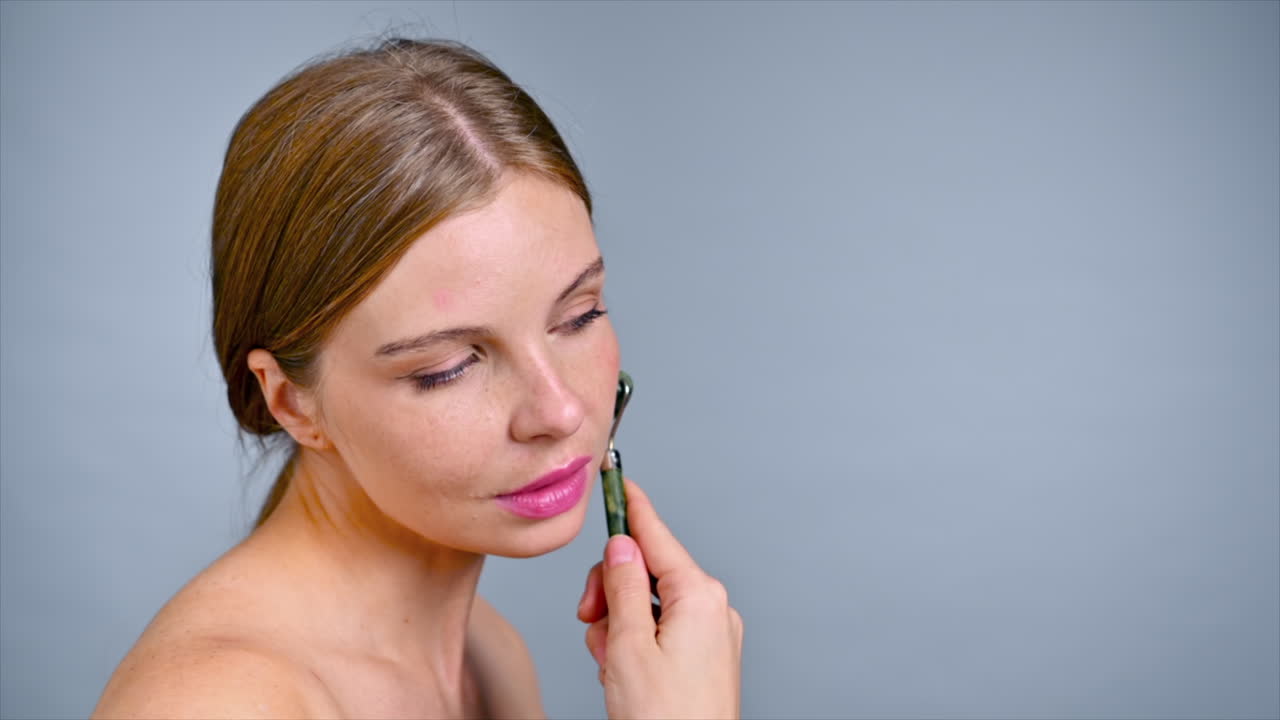 A young caucasian woman is doing facial and neck massage using a roller. Slow motion