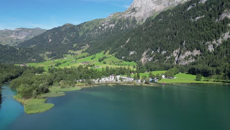 volando sobre un lago limpio hacia un lugar donde hay muchas furgonetas de acampada estacionando personas que van a lugares de vacaciones para alejarse cerca de grandes montañas en verano para esconderse de la sociedad vista natural cinematográfica