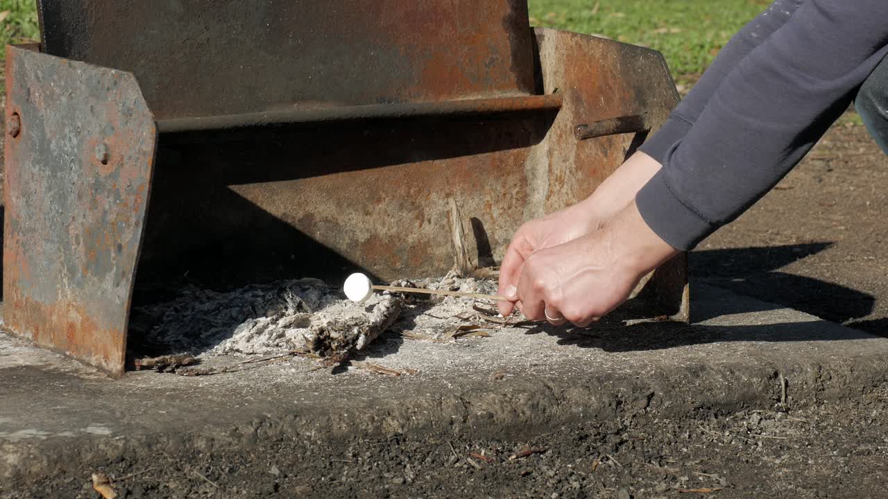 나뭇가지에 달린 뜨거운 재 위에 마시멜로를 요리하는 남자
