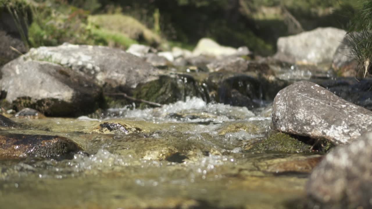 Slowmotion af klar bjergflod der strømmer over sten på en solrig dag