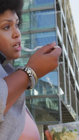 plus size biracial woman walking with smartphone and salad in city