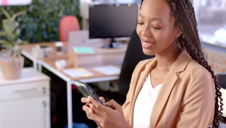 happy african american casual businesswoman using smartphone in office
