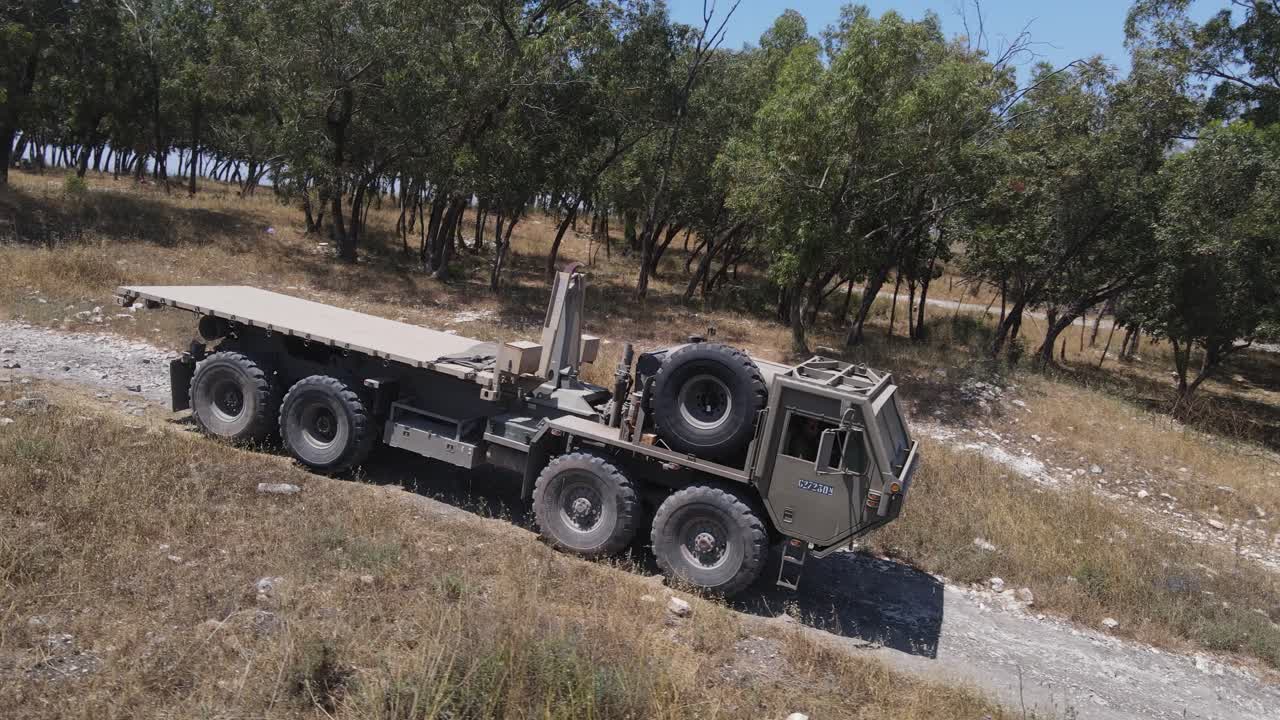 солдаты пехотного отделения израильской армии на автомобиле едут по зеленому полю на учебном полигоне по проселочной дороге, съемка с воздуха