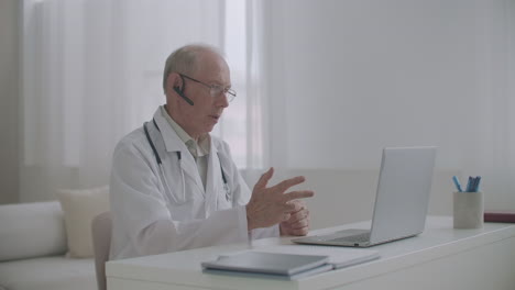 elderly experienced male professor of medicine is lecturing online sitting at office teaching students