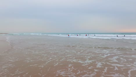 low aerial dolly over low tide waves as surfers carry boards walk to surf break