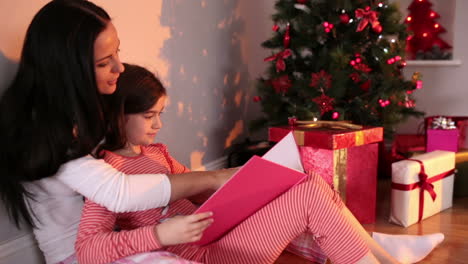 madre leyendo a su hija un cuento junto al árbol de navidad