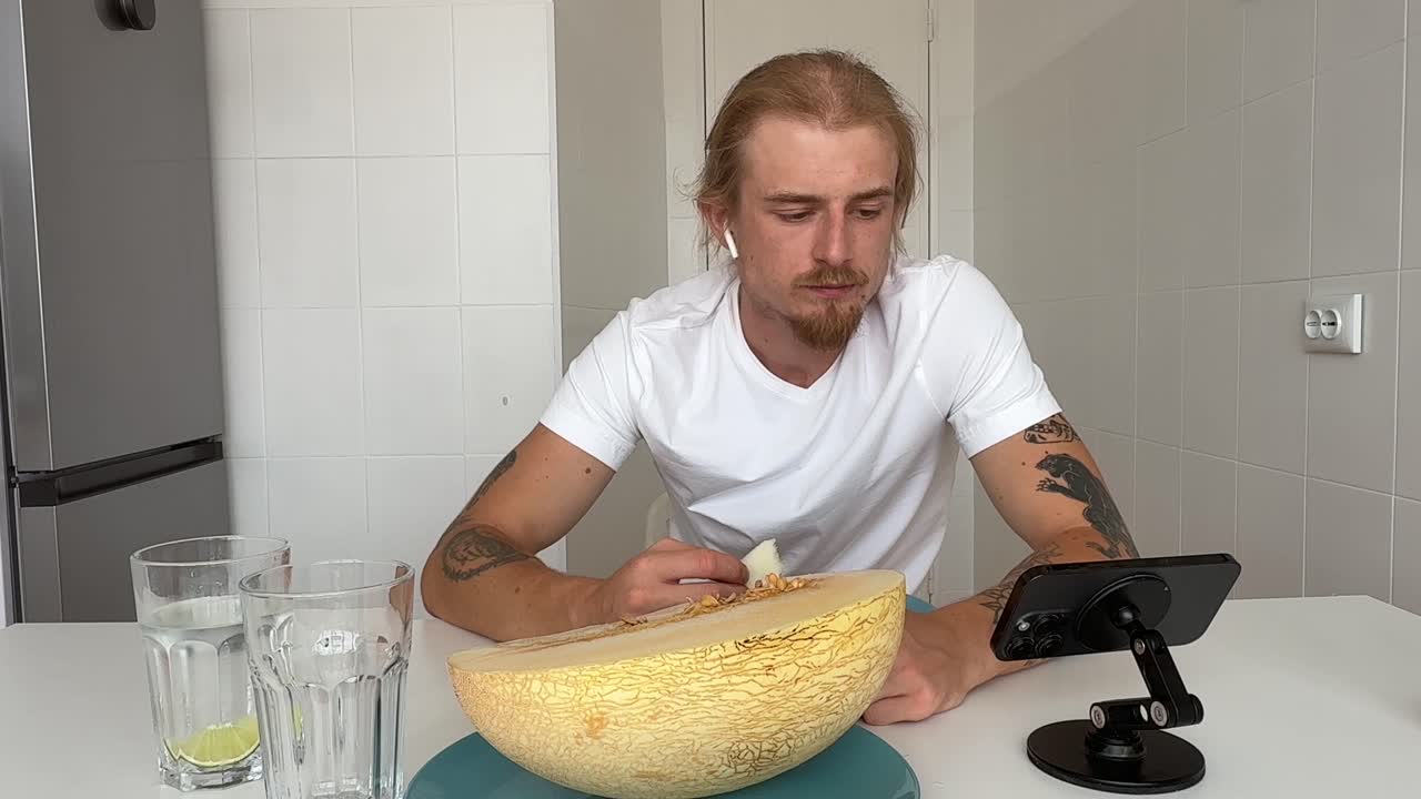 Mann spiser fersk melon på et hvitt kjøkken