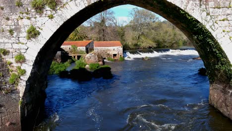 Aerial-View-Of-Old-Water-Mill-With-Dolly-Back-Through-Old-Medieval-Bridge-Over-River-Tambre