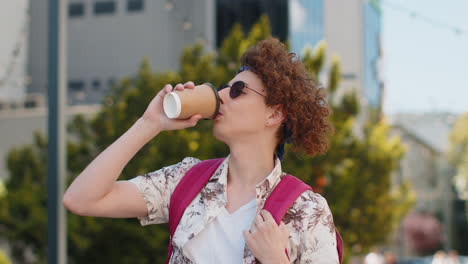 Smiling-man-tourist-enjoying-morning-coffee-hot-drink-relaxing,-taking-a-break-on-urban-city-street