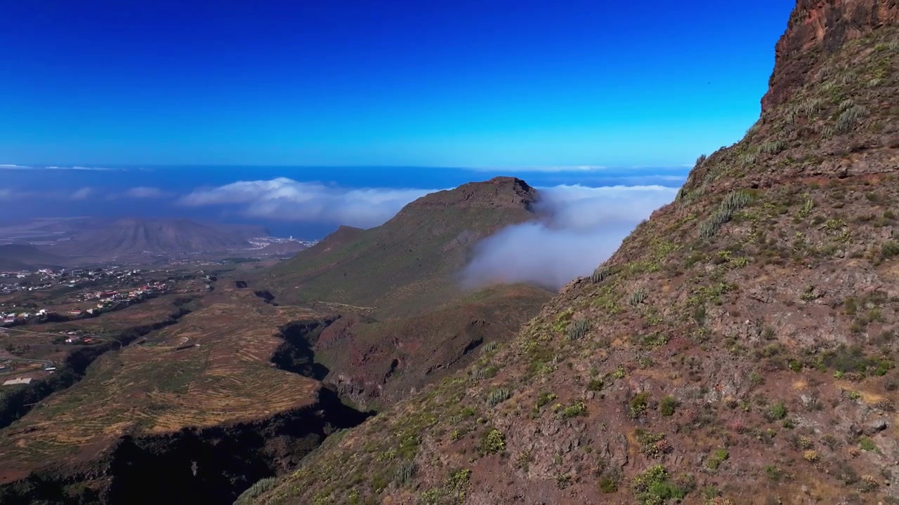 Vista aerea che scivola oltre aspre pendii vulcanici con nuvole che si muovono sopra il Monte Roque Imoque.