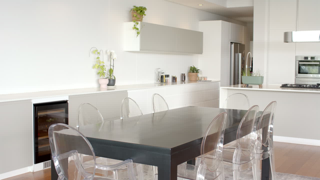 Modern kitchen with transparent chairs around dining table and potted plants, copy space