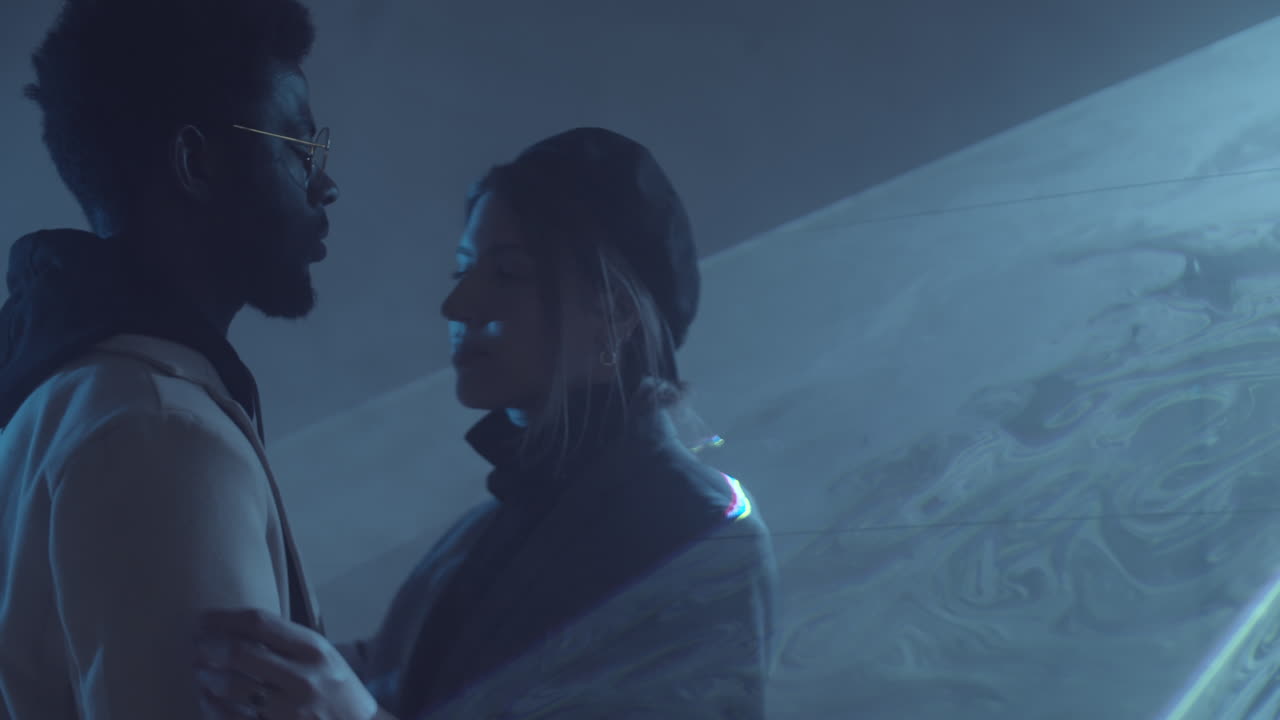 사랑하는 다민족 커플이 레이저 빛으로 어두운 방에서 포옹하고 있습니다.