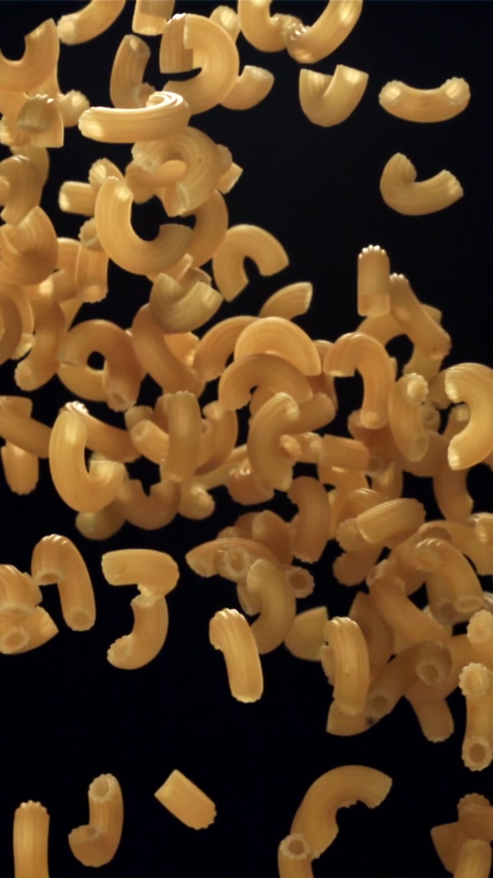Pasta maccheroni secca che cade al rallentatore su sfondo nero.