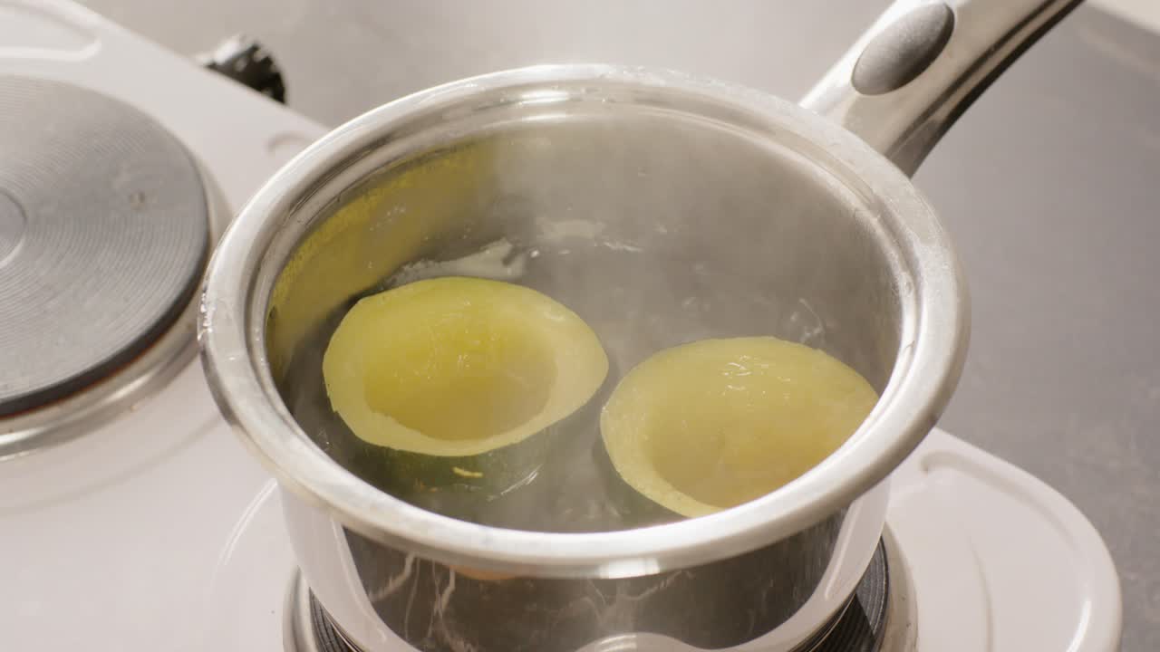 Un fornello elettrico sta scaldando l'acqua in un pentolino, mentre due metà gialle sobbollono per ammorbidirsi sul piano cottura.