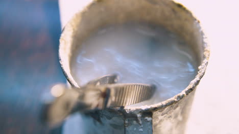 worker-puts-metal-bar-into-container-with-liquid-closeup