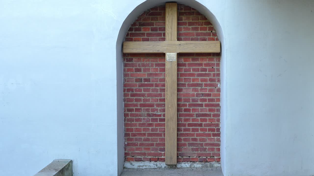 Gradual zoom-in on a large wooden cross mounted on a red brick wall inside a white arched architectural niche.