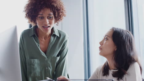 African-American-and-Asian-female-creatives-in-discussion-at-a-computer-in-an-office,-close-up