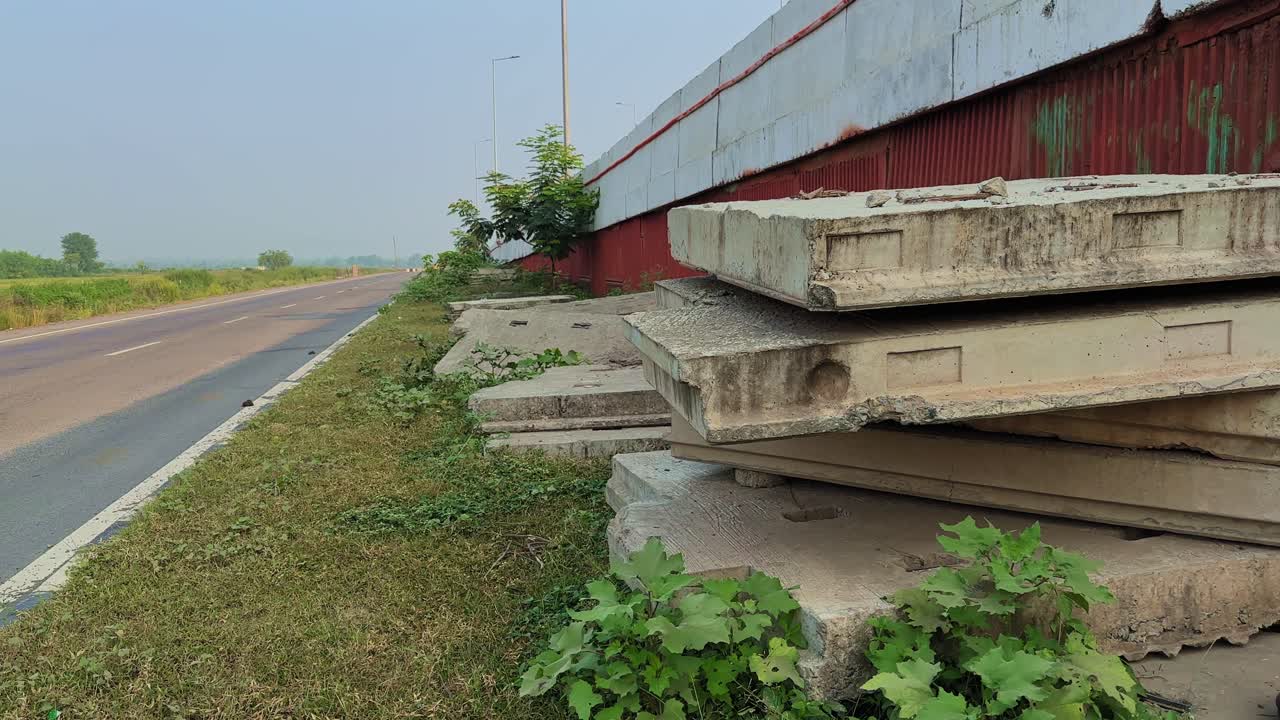 Stacked precast concrete blocks beside a quiet rural highway, used for building an overbridge under clear morning light