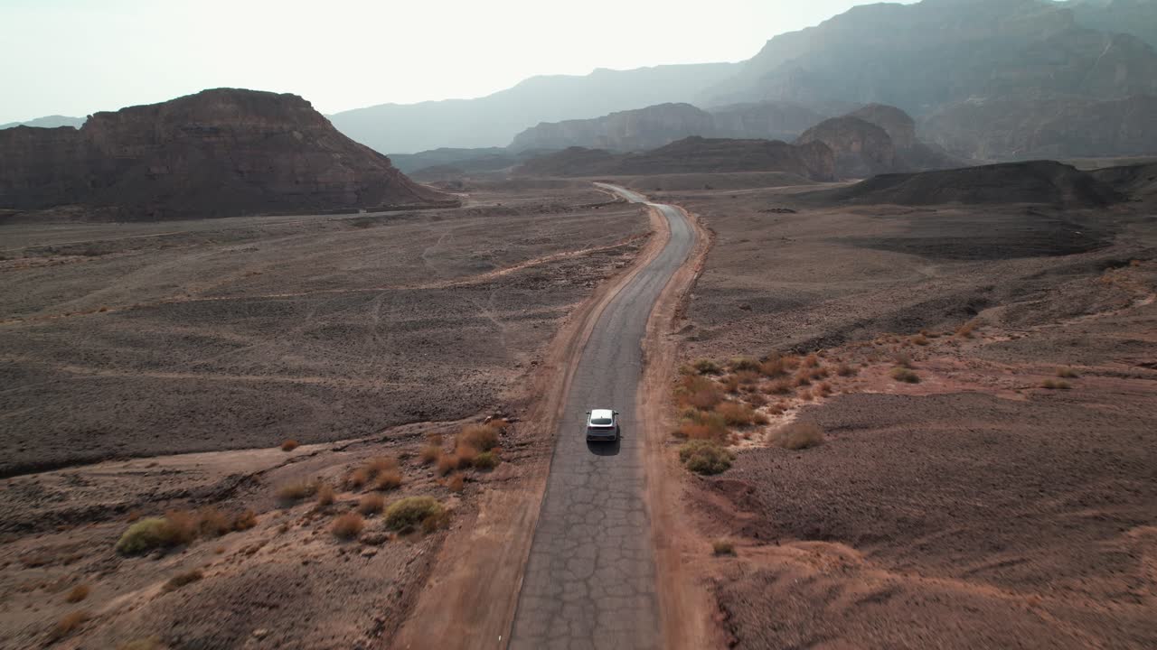 A drone shot following a car driving a path through the desert mountains.
