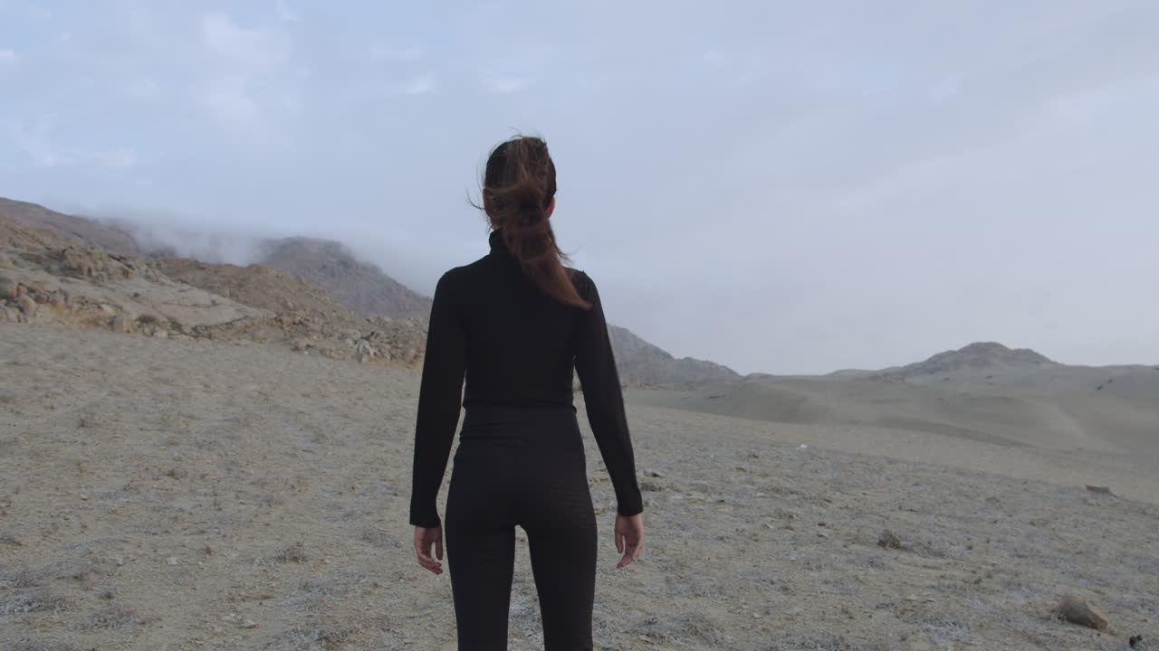 흐린 하늘을 배경으로 오후 사막 한가운데 서 있는 강력한 위치에 있는 여성의 백샷