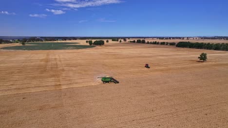 High-shot-moving-alongside-a-harvester-working-in-a-paddock-with-dust-coming-from-behind