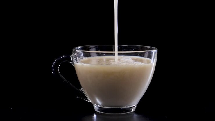 Milk streams into a glass cup of tea, creating swirling patterns. Captured against a black background with dramatic lighting