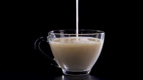 milk streams into a glass cup of tea, creating swirling patterns. captured against a black background with dramatic lighting