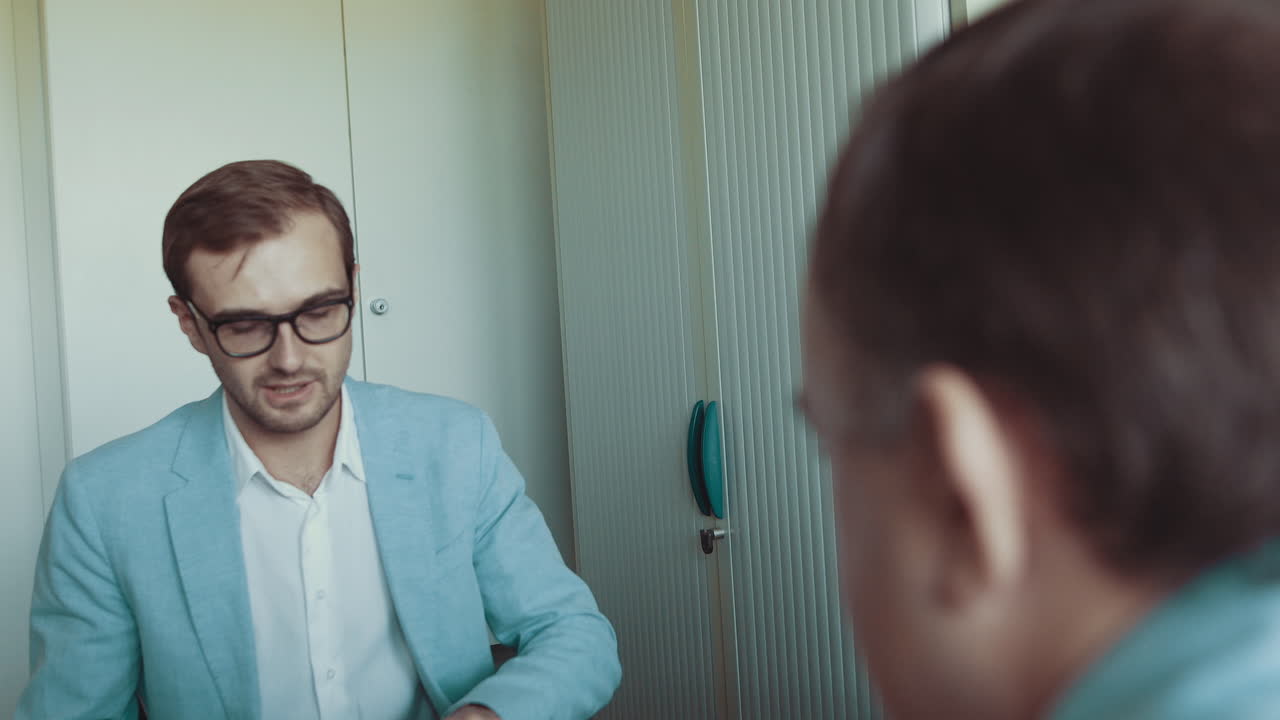 Jovem bonito de óculos, um funcionário de sucesso, trabalha com documentos; o homem está sentado no escritório.