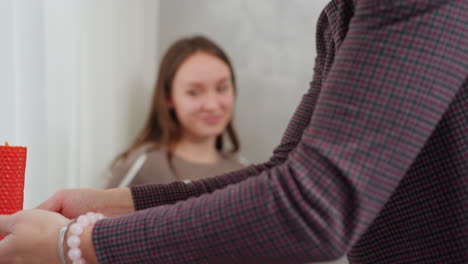 primer plano de manos femeninas sosteniendo una elegante vela roja en un soporte de vidrio, adornada con una delicada pulsera de cuentas, iluminación suave y fondo borroso