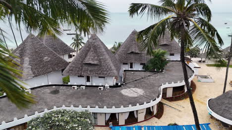 thatched roof villas on resort town accommodations at nungwi beach in zanzibar, africa, tanzania. aerial drone shot
