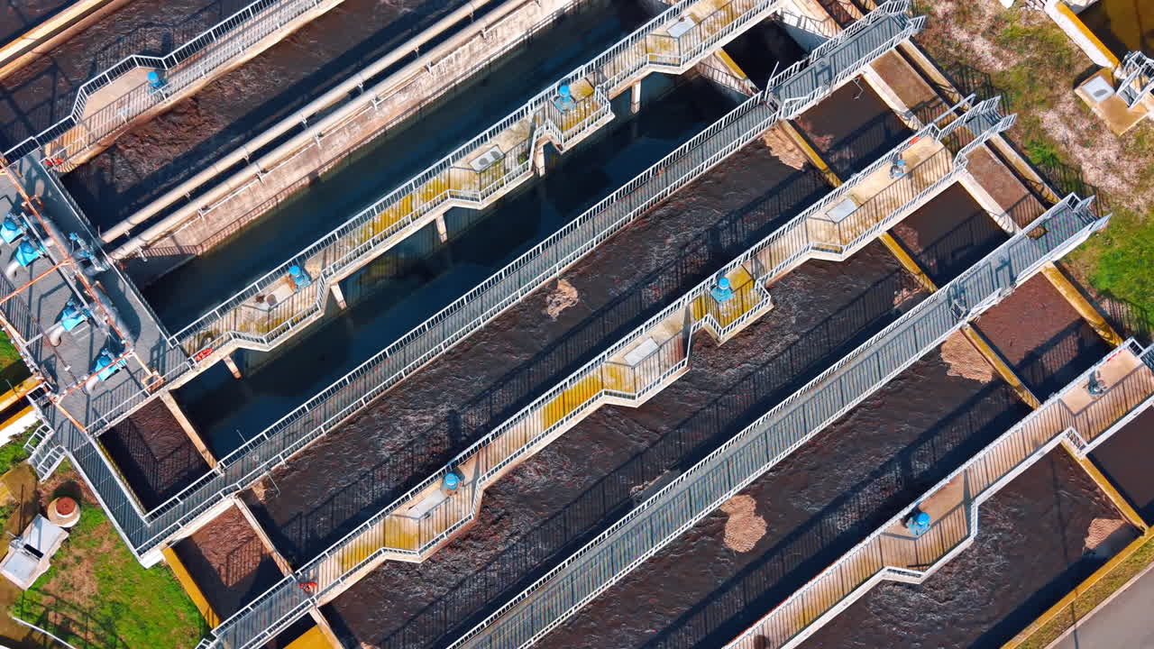 High angle view of rectangular aeration tanks with foam. Close up aerial perspective of long rectangular aeration basins with moving wastewater and metal walkways