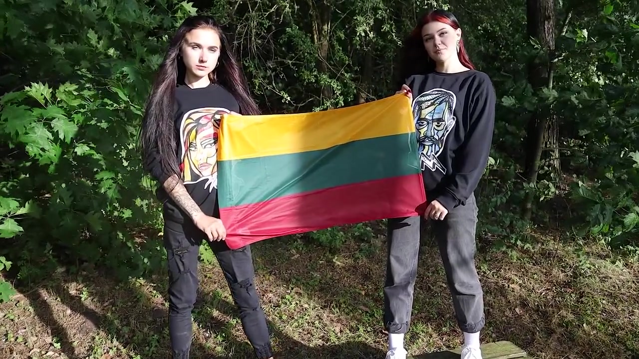 Due ragazze che tengono in alto una bandiera lituana nella foresta.